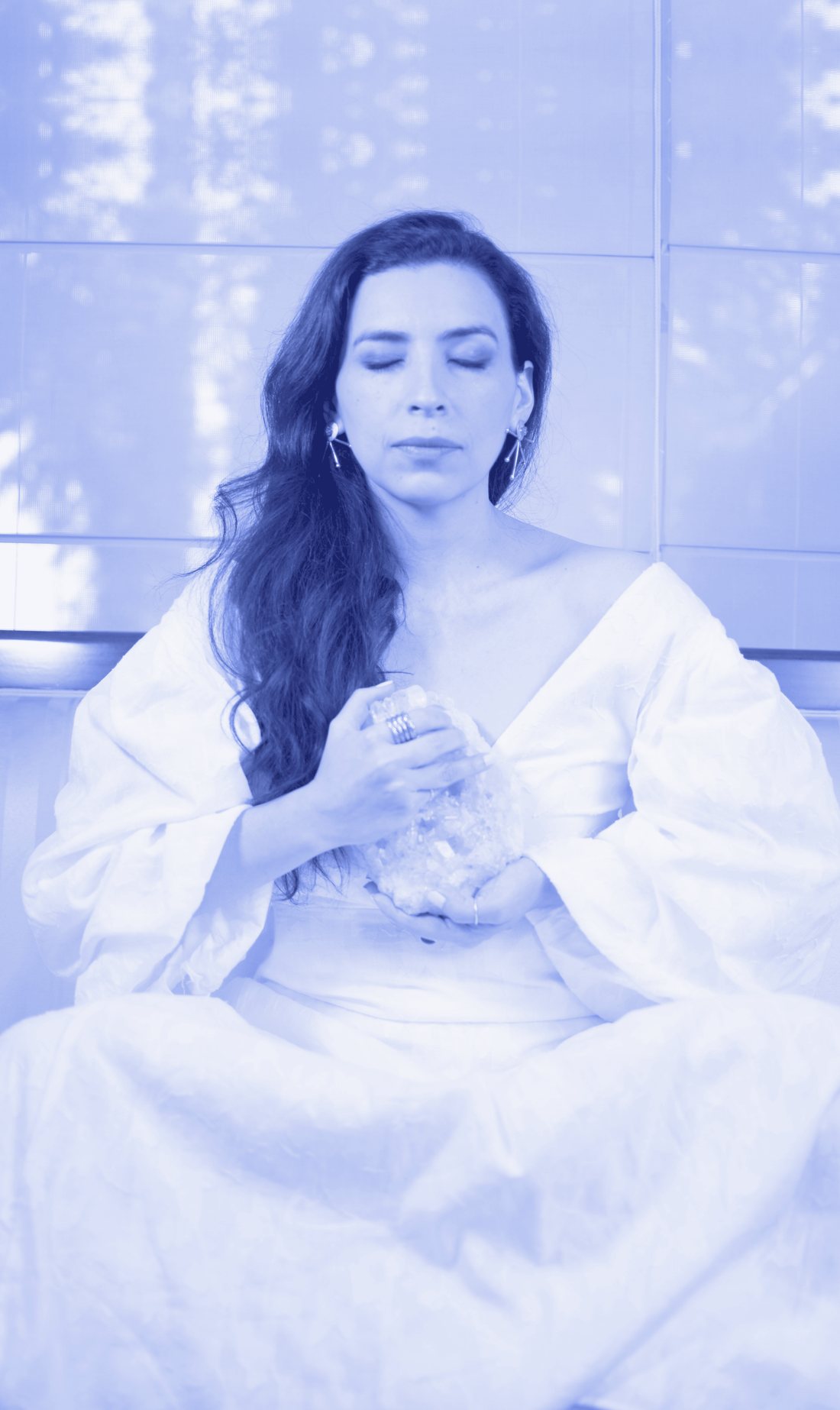 Odette, sentada con los ojos cerrados, sostiene un cuarzo entre las manos